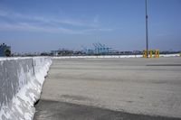 a large white wall in the middle of a parking lot near a harbor with ships