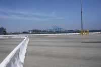 a large white wall in the middle of a parking lot near a harbor with ships