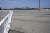 a large white wall in the middle of a parking lot near a harbor with ships