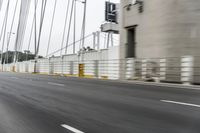 a gray car driving over a bridge with lights on in the distance, the bridge and trees near