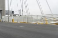 a gray car driving over a bridge with lights on in the distance, the bridge and trees near