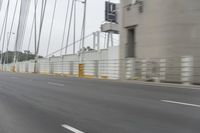 a gray car driving over a bridge with lights on in the distance, the bridge and trees near