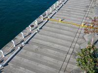 a view of a walkway with white railings next to the water and a yellow arrow pointing right down towards it