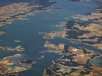 a landscape is seen from the air with a small plane in the distance and blue water on the far side