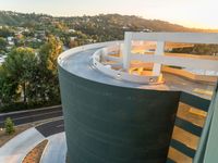 a building with a curved balcony at the top of it near trees and a sunset