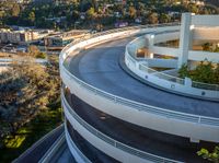 large curved concrete ramp in a modern city with a hillside in the background and trees on the side