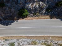 a motorcycle rider rides past a rock cliff on the mountain road from above a city