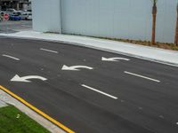 a paved street with four white arrows next to palm trees on the side of the road