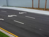 a paved street with four white arrows next to palm trees on the side of the road