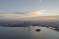 a body of water near a big city and a large island at sunset time and clouds above