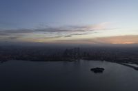 a body of water near a big city and a large island at sunset time and clouds above