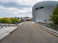 a bridge leading to a building with a curved roof on top of it and a few cars driving by