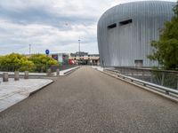 a bridge leading to a building with a curved roof on top of it and a few cars driving by