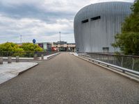 a bridge leading to a building with a curved roof on top of it and a few cars driving by