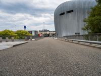 a bridge leading to a building with a curved roof on top of it and a few cars driving by