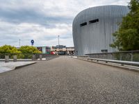 a bridge leading to a building with a curved roof on top of it and a few cars driving by