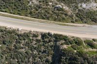 an aerial view of a person riding a motorcycle on the road below trees and a mountain