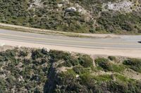 an aerial view of a person riding a motorcycle on the road below trees and a mountain