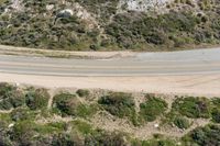 an aerial view of a person riding a motorcycle on the road below trees and a mountain