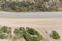 an aerial view of a person riding a motorcycle on the road below trees and a mountain