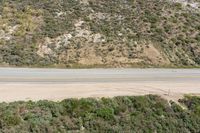 an aerial view of a person riding a motorcycle on the road below trees and a mountain