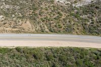 an aerial view of a person riding a motorcycle on the road below trees and a mountain