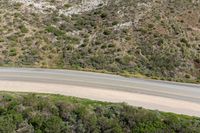 an aerial view of a person riding a motorcycle on the road below trees and a mountain