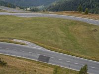 a car is driving on an empty road near a hill with trees and mountains in the distance