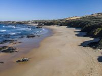 a sandy beach with a little ocean next to it, next to a hill, with a building on the far shore