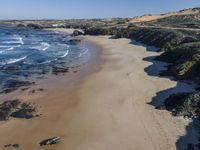 a sandy beach with a little ocean next to it, next to a hill, with a building on the far shore