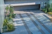 there is an empty courtyard with many plants growing on the side of it and a building behind it