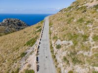 paved walkway on mountain above a grassy cliff and ocean views over the water as seen from the top