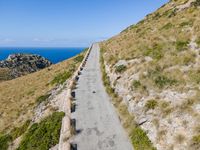 paved walkway on mountain above a grassy cliff and ocean views over the water as seen from the top