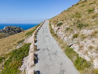 paved walkway on mountain above a grassy cliff and ocean views over the water as seen from the top