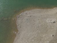 an aerial view of people wading in the water near shore rocks and sand with a paddle board