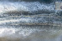 an aerial view of a person on a surfboard riding waves in the ocean waters