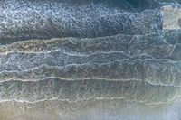 an aerial view of a person on a surfboard riding waves in the ocean waters