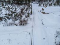 overhead view of tracks in deep snow near forest filled with trees and shrubs with trees on hillside at top