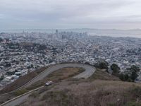 a winding road down a hillside to a big city skyline with lots of tall buildings