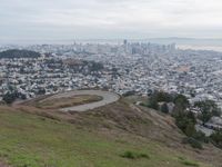 a winding road down a hillside to a big city skyline with lots of tall buildings