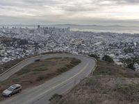 a winding road down a hillside to a big city skyline with lots of tall buildings