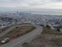 a winding road down a hillside to a big city skyline with lots of tall buildings