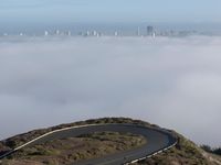 an image of clouds and city below the road in the hills above it, with a car traveling on one