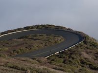 an image of clouds and city below the road in the hills above it, with a car traveling on one