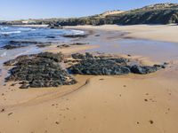 a sandy beach with rock formations in the middle of it and people walking along the shore