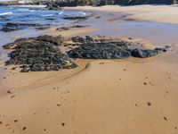 a sandy beach with rock formations in the middle of it and people walking along the shore