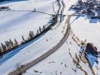 an aerial photo showing a roadway in the middle of a snowy countryside, on top of a hill