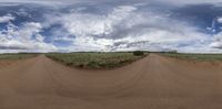 there is a wide angle view of the dirt road near the trees and clouds in the blue sky