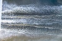 a surfer on an ocean wave rolls around in the distance with the surfboard in focus