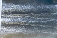 a surfer on an ocean wave rolls around in the distance with the surfboard in focus